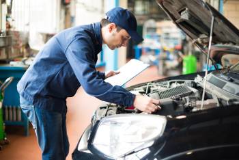Mechanic with checklist looks over car engine in service garage
