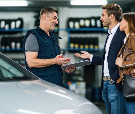 Auto service specialist discussing details of service job with clients in auto repair shop