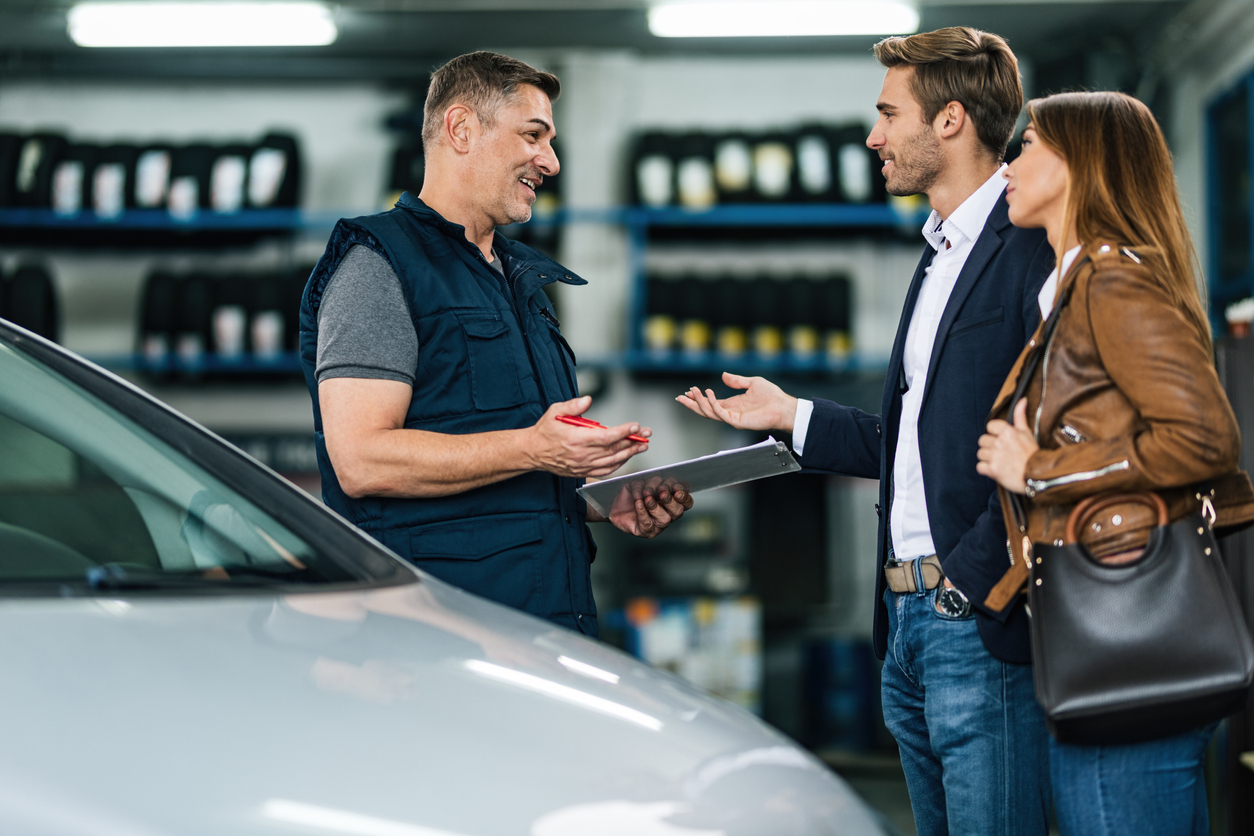 Auto service specialist discussing details of service job with clients in auto repair shop